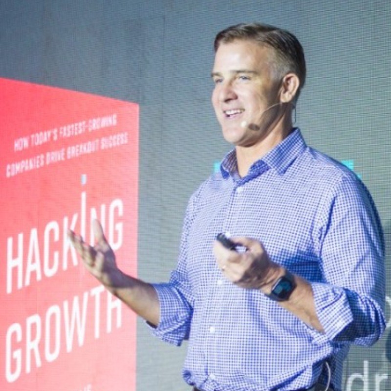 Sean Ellis em palestra com o livro Hacking growth ao fundo